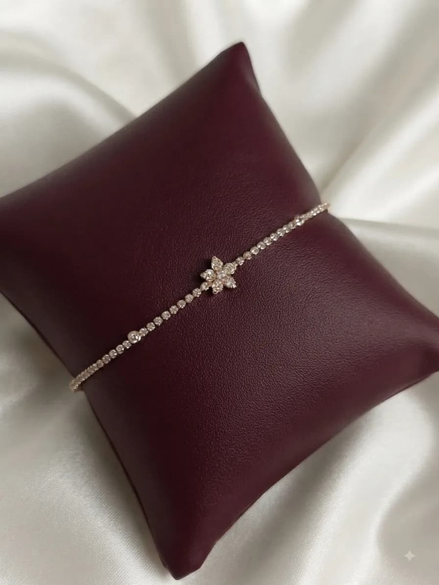 A slim gold-plated tennis bracelet with a crystal flower at its centre, on an oxblood cushion