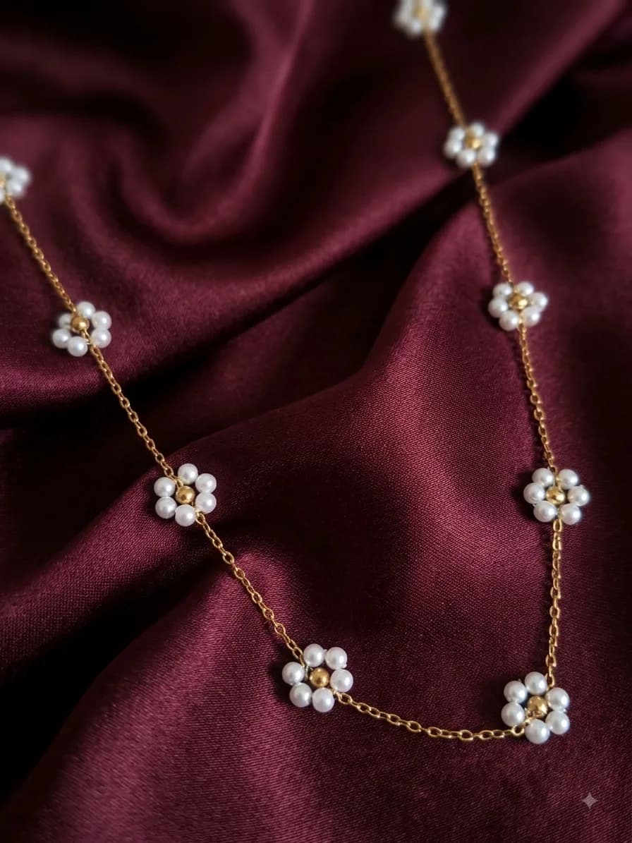 A gold-plated chain necklace strung with pearl flowers, laid on oxblood satin