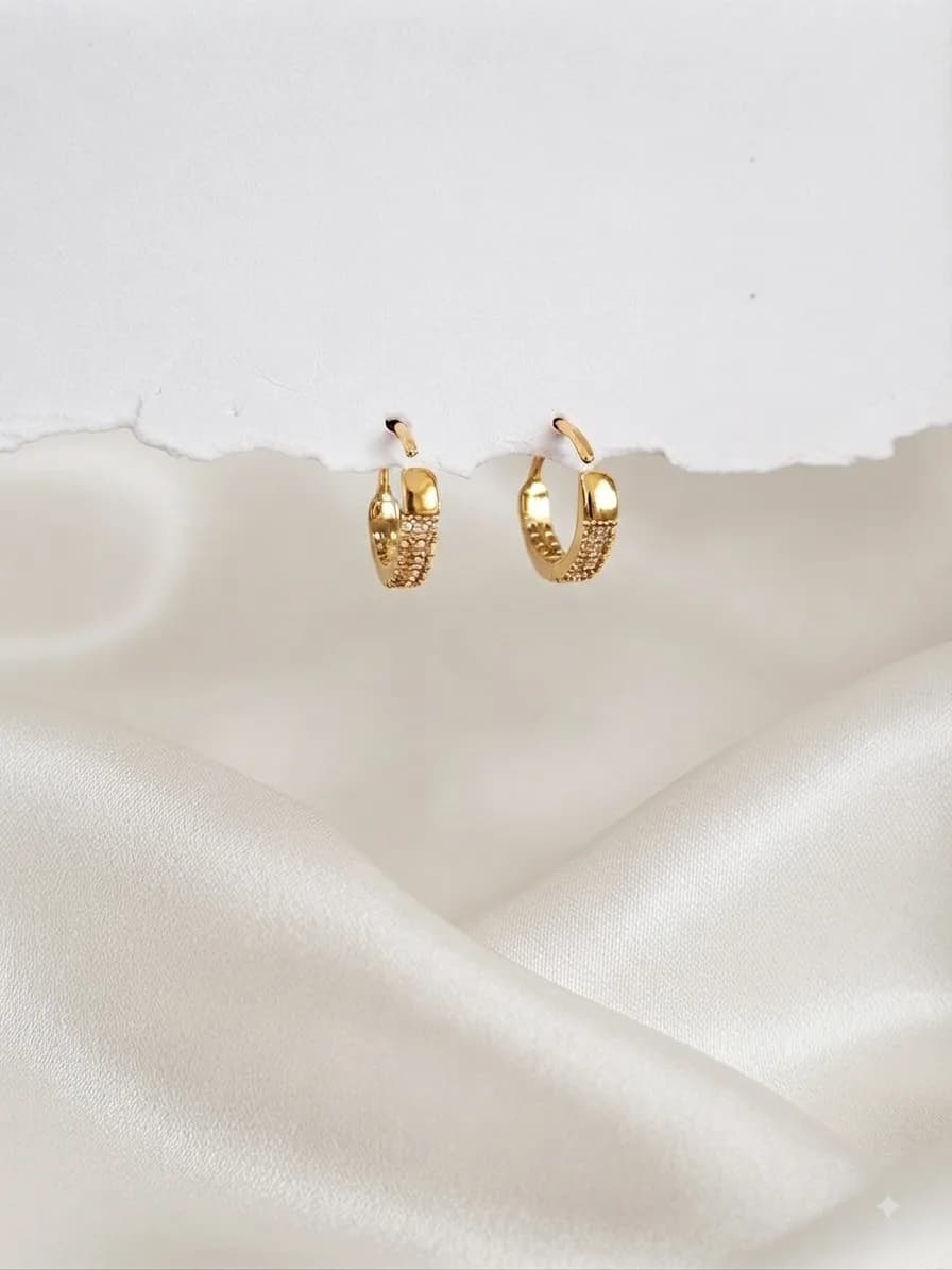 A pair of tiny gold-plated hoops pavé-set with clear stones, on ivory satin