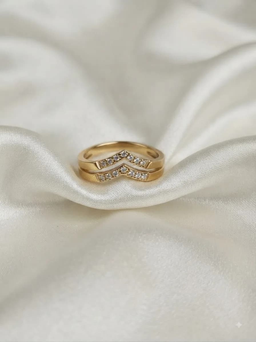 Two gold-plated bands, one set with clear stones in a chevron, on ivory satin
