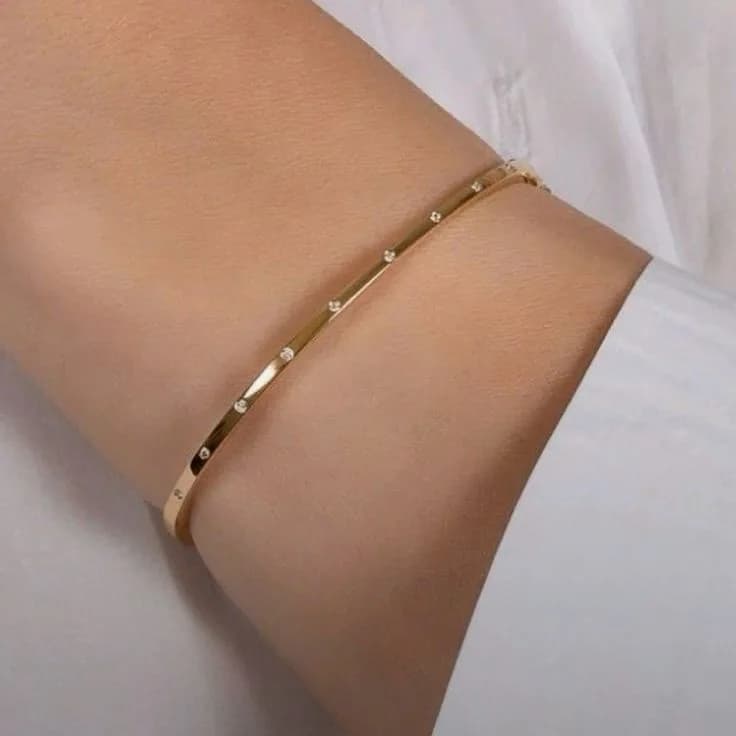A slim gold-plated bangle scattered with tiny clear stones, worn over a white cuff