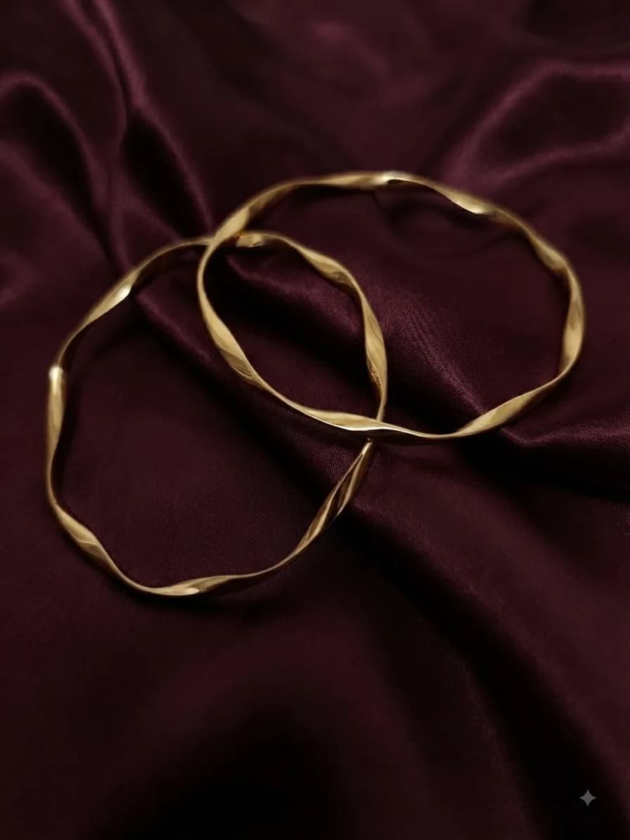 Two twisted gold-plated bangles with a wave through the metal, on oxblood satin