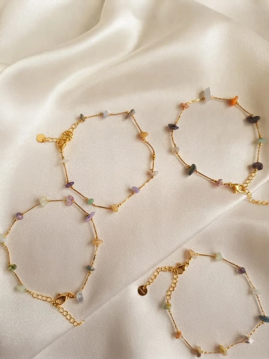 Four gold-plated chain bracelets strung with coloured stone beads, laid out on ivory satin
