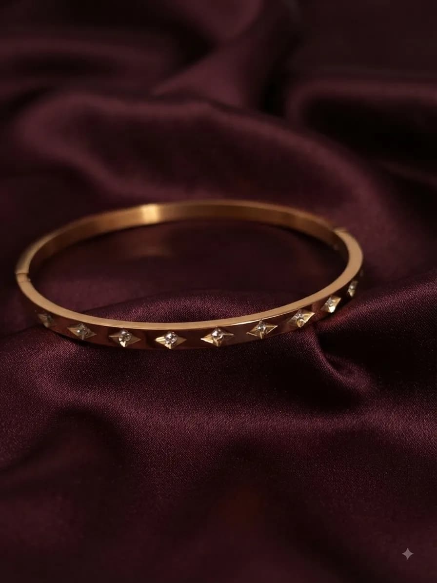 A slim gold-plated bangle set with small star motifs, on oxblood satin