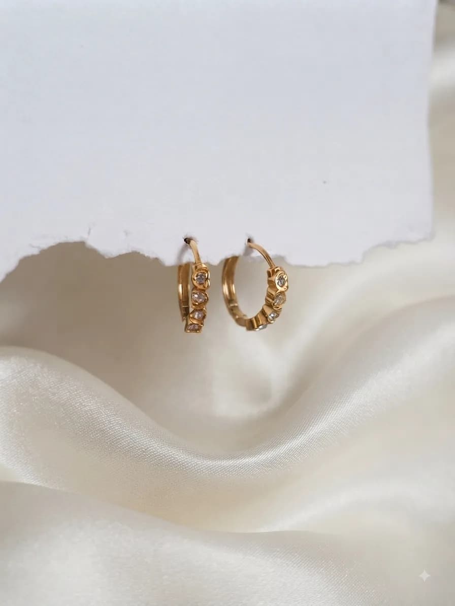 A pair of small gold-plated hoops pavé-set with clear stones, on ivory satin