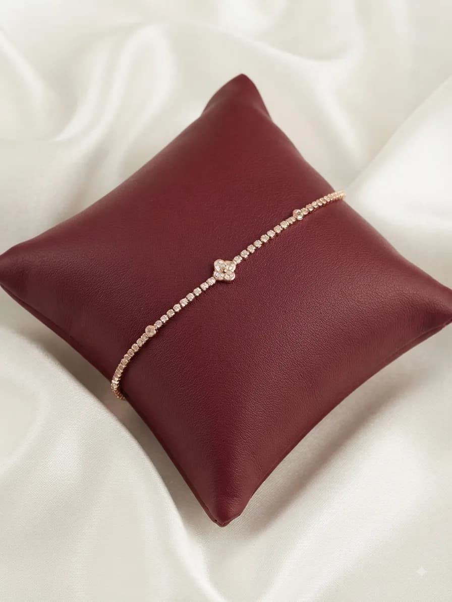 A slim clear-stone line bracelet with a clover motif at its centre, on an oxblood cushion