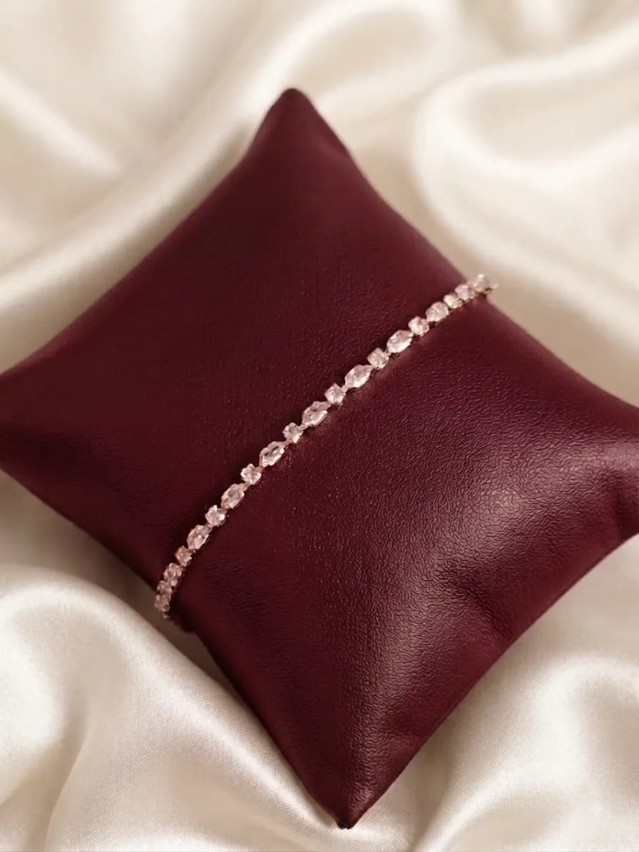 A line of graduated clear stones in gold-plated settings, on an oxblood cushion