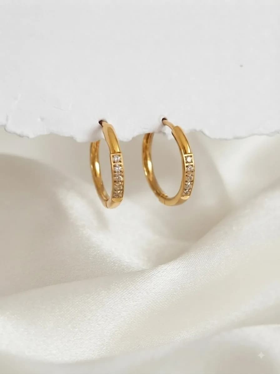 A pair of gold-plated hoops with a line of clear stones along the front, on ivory satin