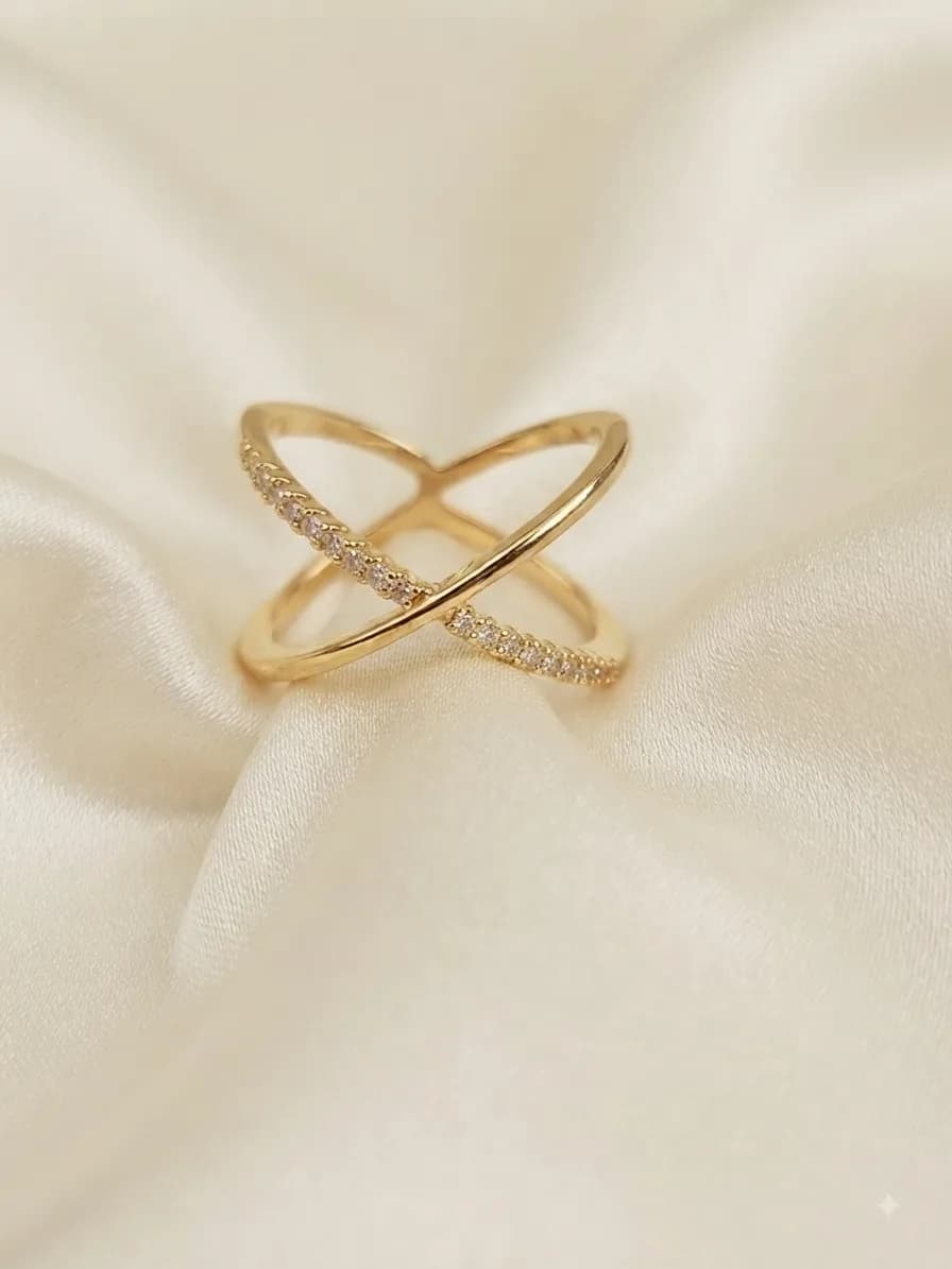 A gold-plated ring of two crossing bands, one pavé-set with clear stones, on ivory satin