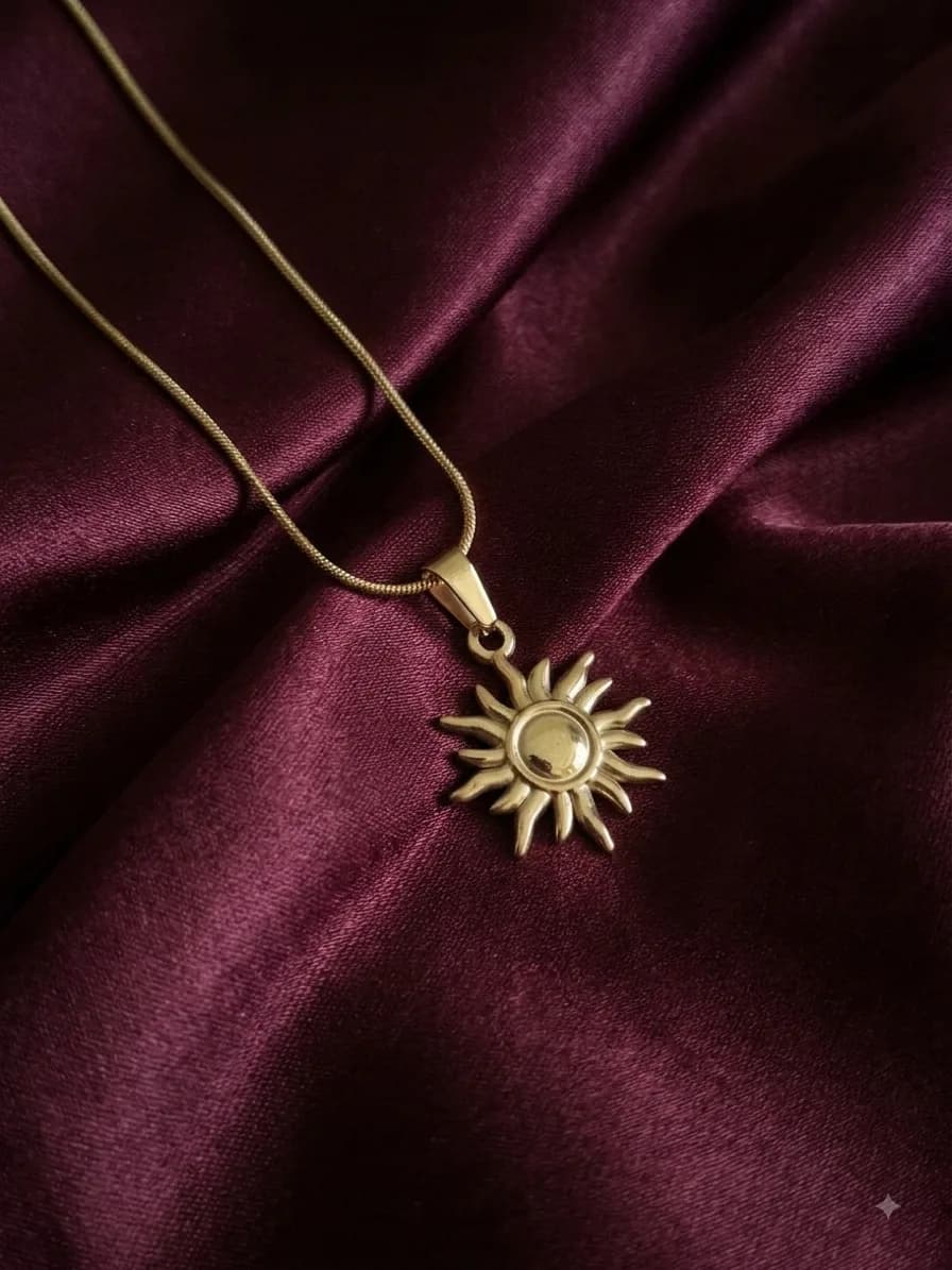 A flat gold-plated chain with a sunburst pendant around a domed centre, on oxblood satin