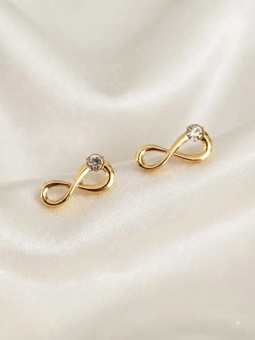 A pair of gold-plated infinity-loop studs finished with a clear stone, on ivory satin
