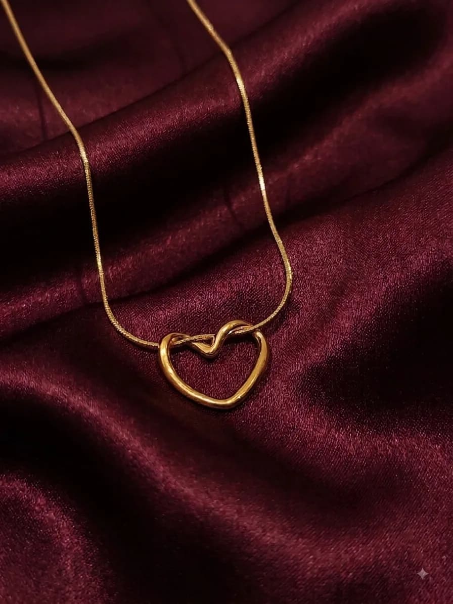 A flat gold-plated snake chain with an open heart outline pendant, on oxblood satin