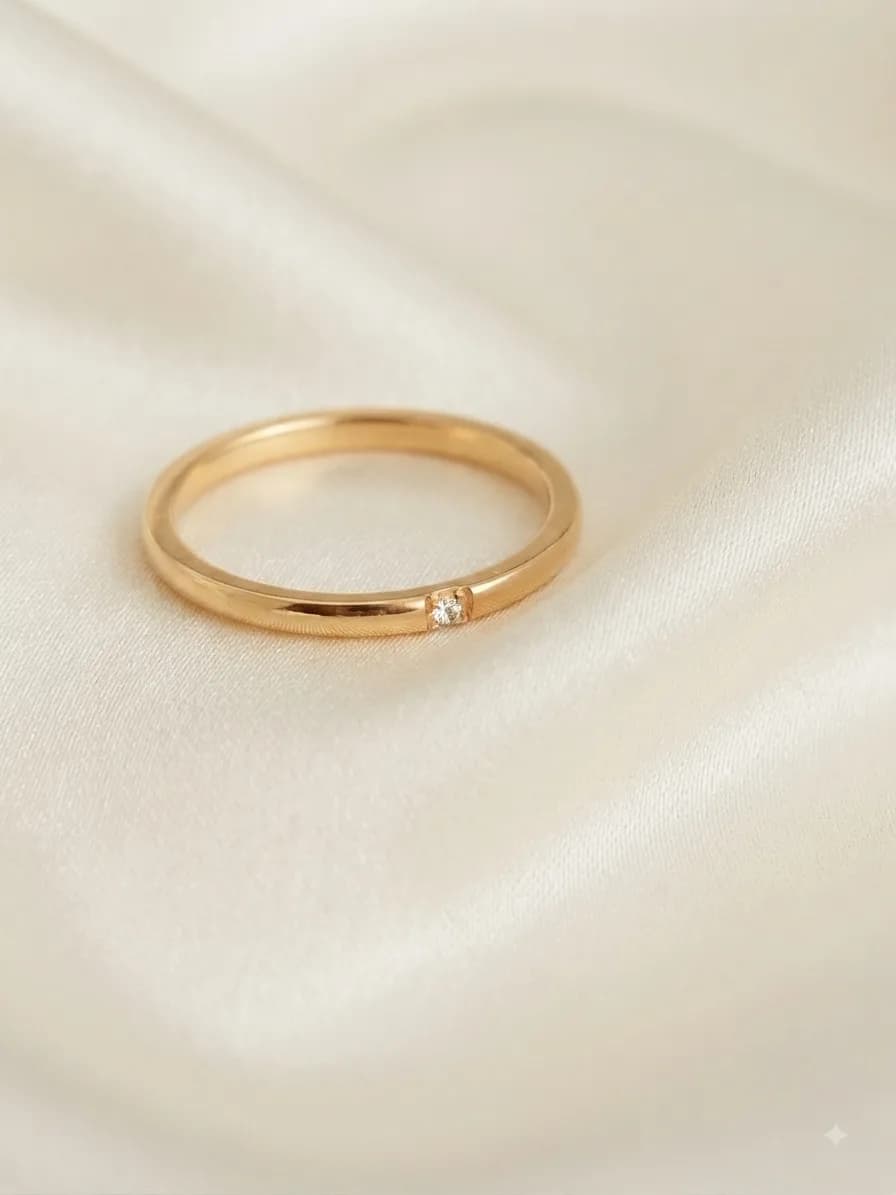 A slim plain gold-plated band with a single stone set flush into it, on ivory satin