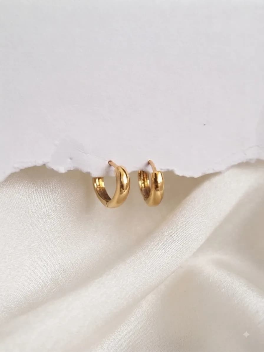 A pair of small plain gold-plated huggie hoops on ivory satin