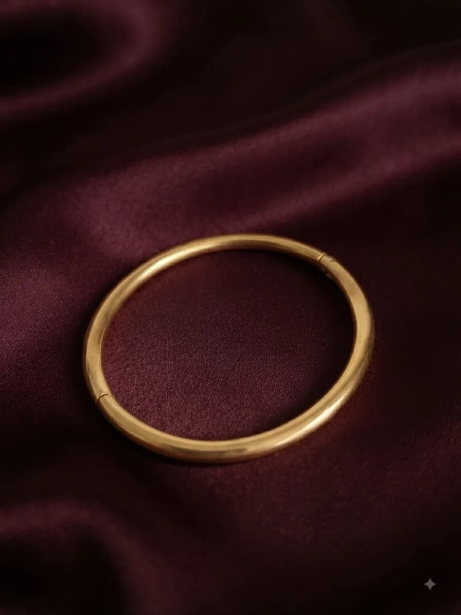 A plain polished gold-plated bangle, on oxblood satin