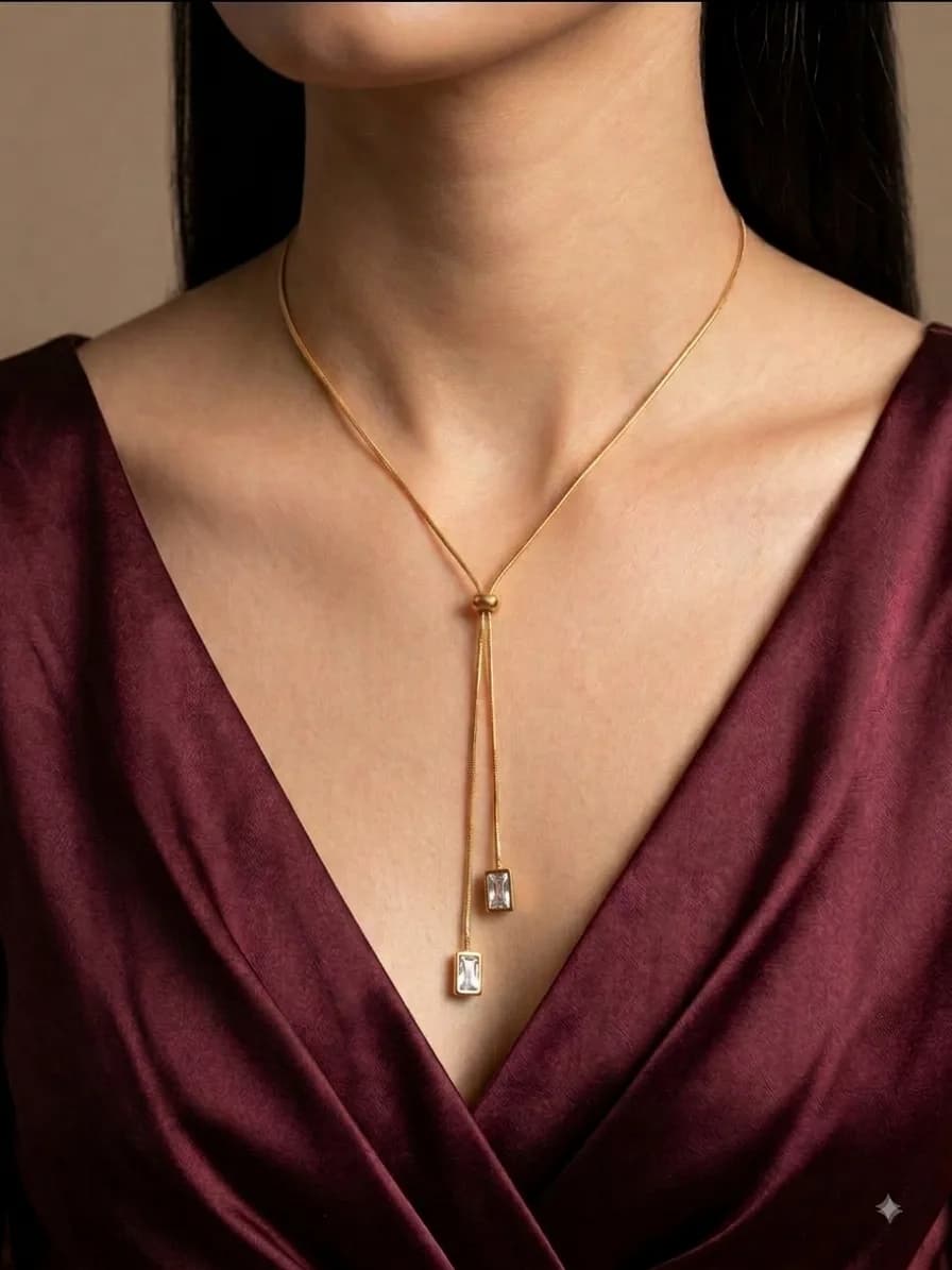 A model wearing a gold-plated lariat necklace whose two sliding ends finish in clear baguette stones