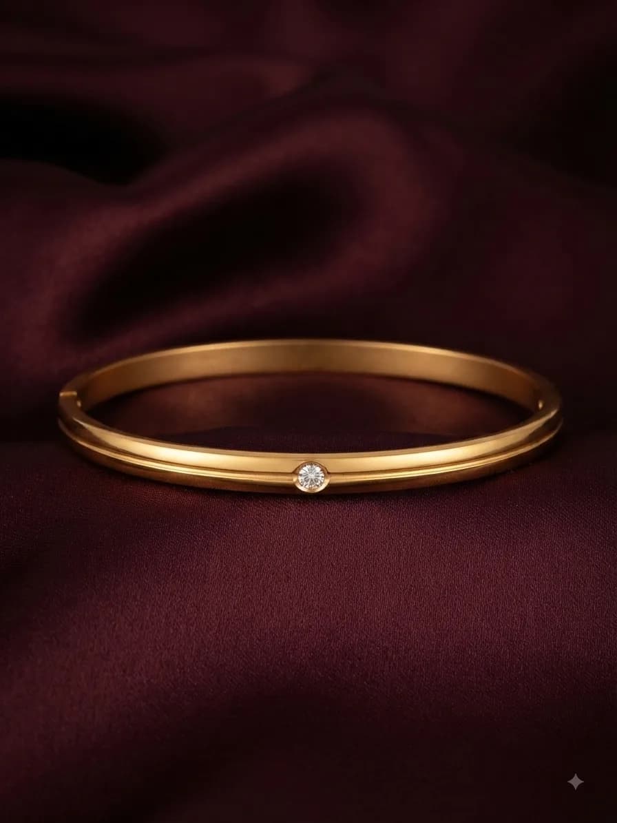 A plain gold-plated bangle holding a single clear stone at its centre, on oxblood satin