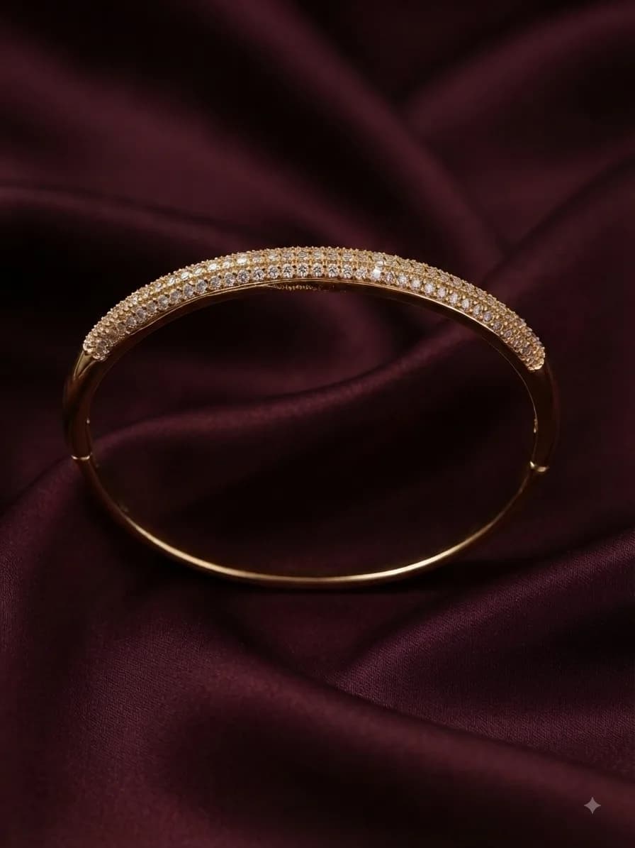 A gold-plated bangle pavé-set with clear stones across the top, on oxblood satin