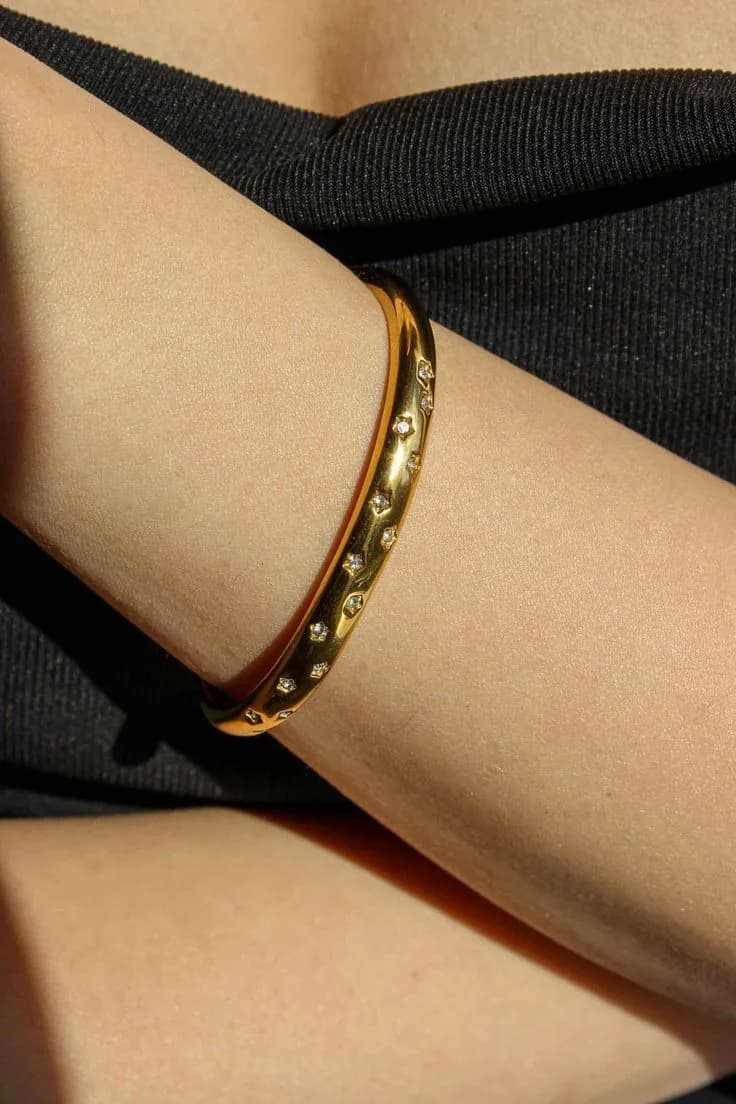 Two gold-plated bangles, one dusted with small stones, worn against a black sleeve