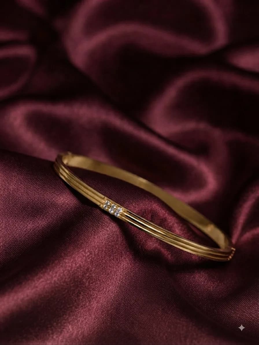 A slim gold-plated bangle with a line of clear pavé stones along one side, on oxblood satin
