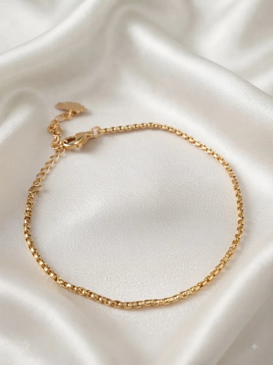 A gold-plated rope chain bracelet coiled on ivory satin, its extender chain trailing