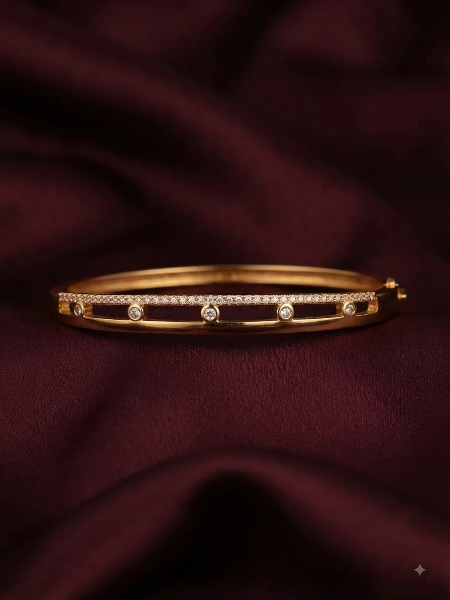 A gold-plated bangle with clear stones spaced along a channel, on oxblood satin