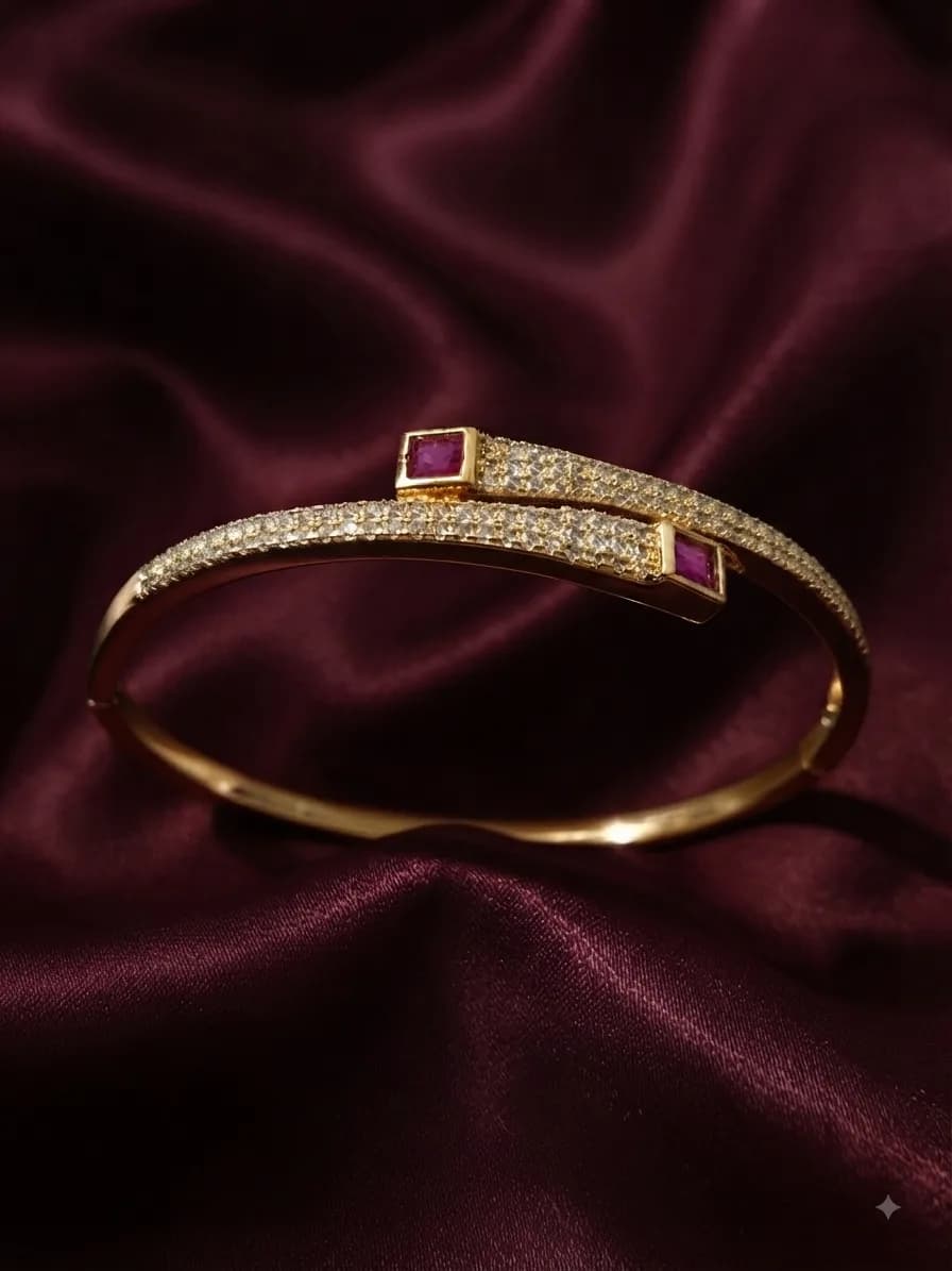 A gold-plated bangle pavé-set with clear stones between two square rubies, on oxblood satin