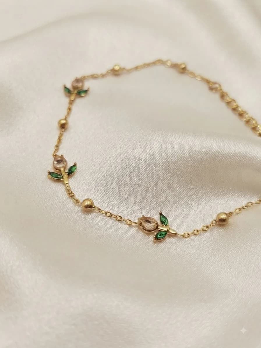 A gold-plated chain bracelet with green enamel leaves and small rose stations, on ivory satin